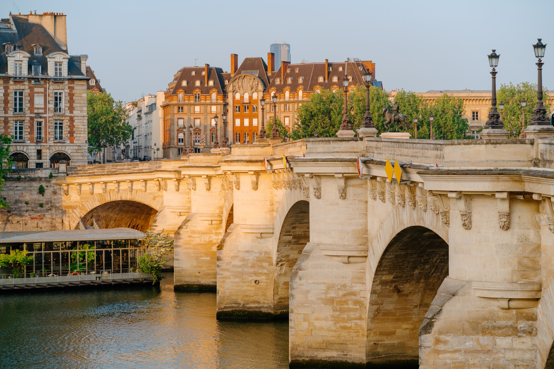 View of the Pont Neuf at sunrise, the Seine, and a boat filled with trees on the water, at Pont Neuf, Paris.