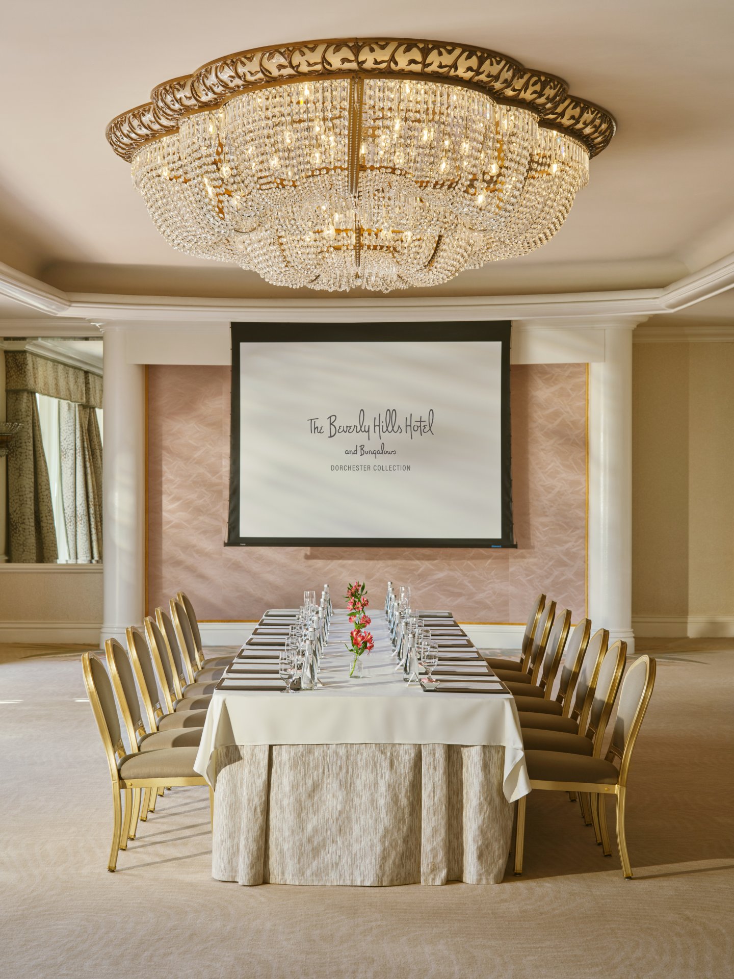 Chandelier-lit meeting room with a long table, chairs, and a presentation screen in elegant setting