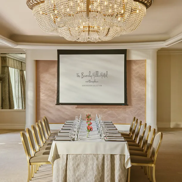 Chandelier-lit meeting room with a long table, chairs, and a presentation screen in elegant setting