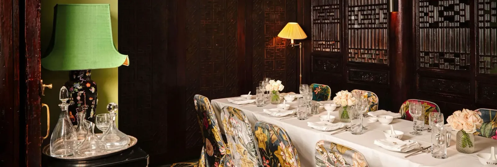 Private dining space at China Tang at The Dorchester, showcasing a beautifully dressed banquet table with fine china, crystal glassware and fresh floral arrangements, surrounded by vibrant embroidered chairs and intricate dark wood screens.