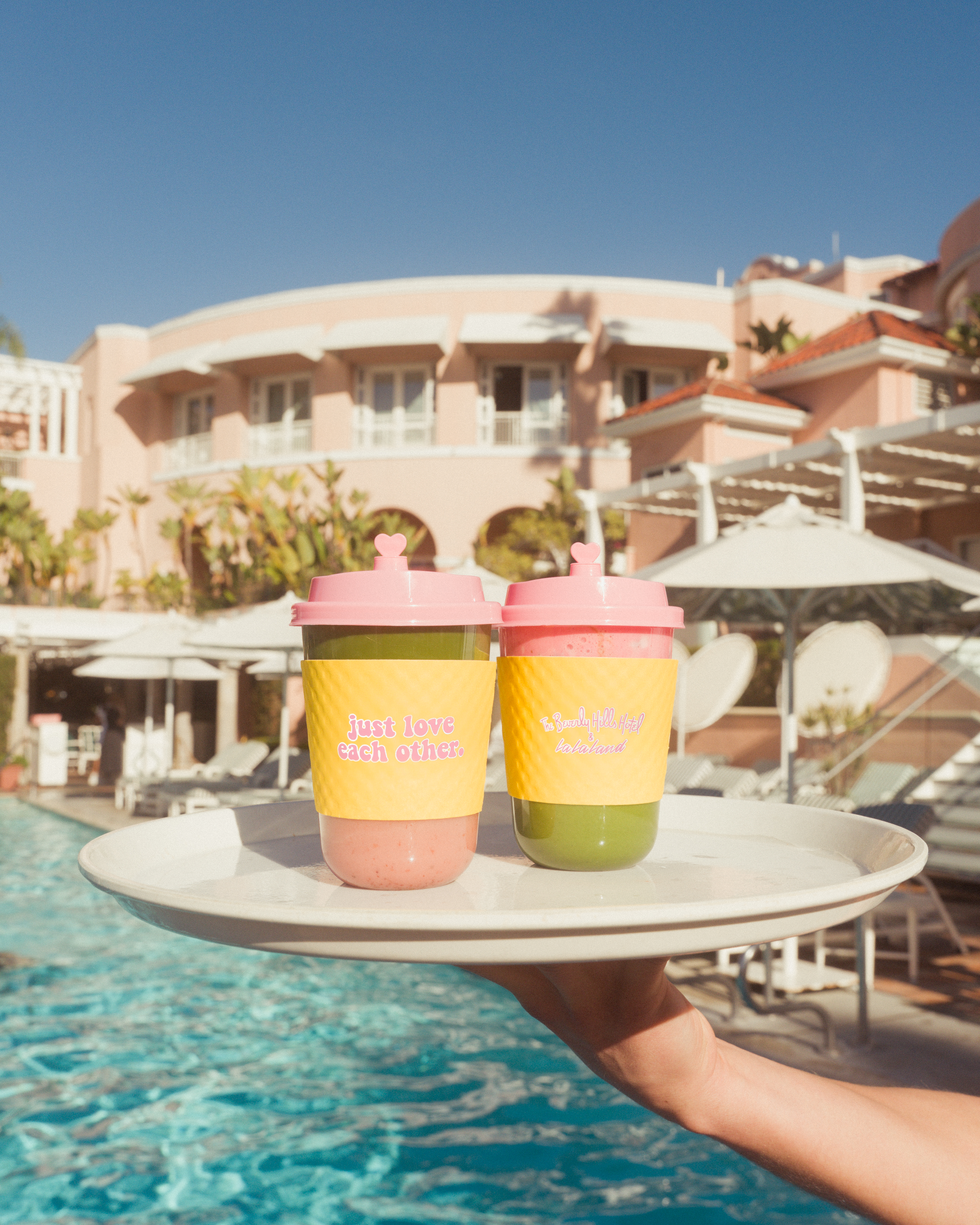 Two matcha lattes on a tray in front of the Beverly Hills Hotel pool with hotel in background and blue skies