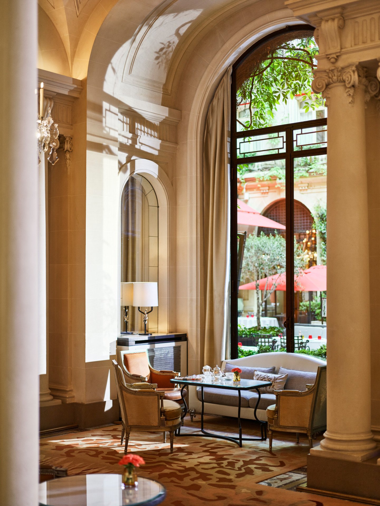 Mesa de jantar na galeria, mesa com chávenas de chá, dois cadeirões e um sofá junto a uma janela solarenga com vista para o jardim do pátio, no Hôtel Plaza Athénée, Paris