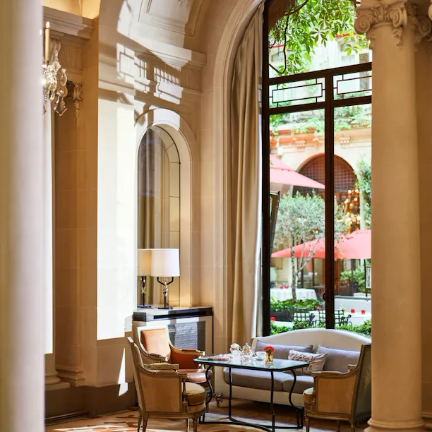 Mesa de jantar na galeria, mesa com chávenas de chá, dois cadeirões e um sofá junto a uma janela solarenga com vista para o jardim do pátio, no Hôtel Plaza Athénée, Paris