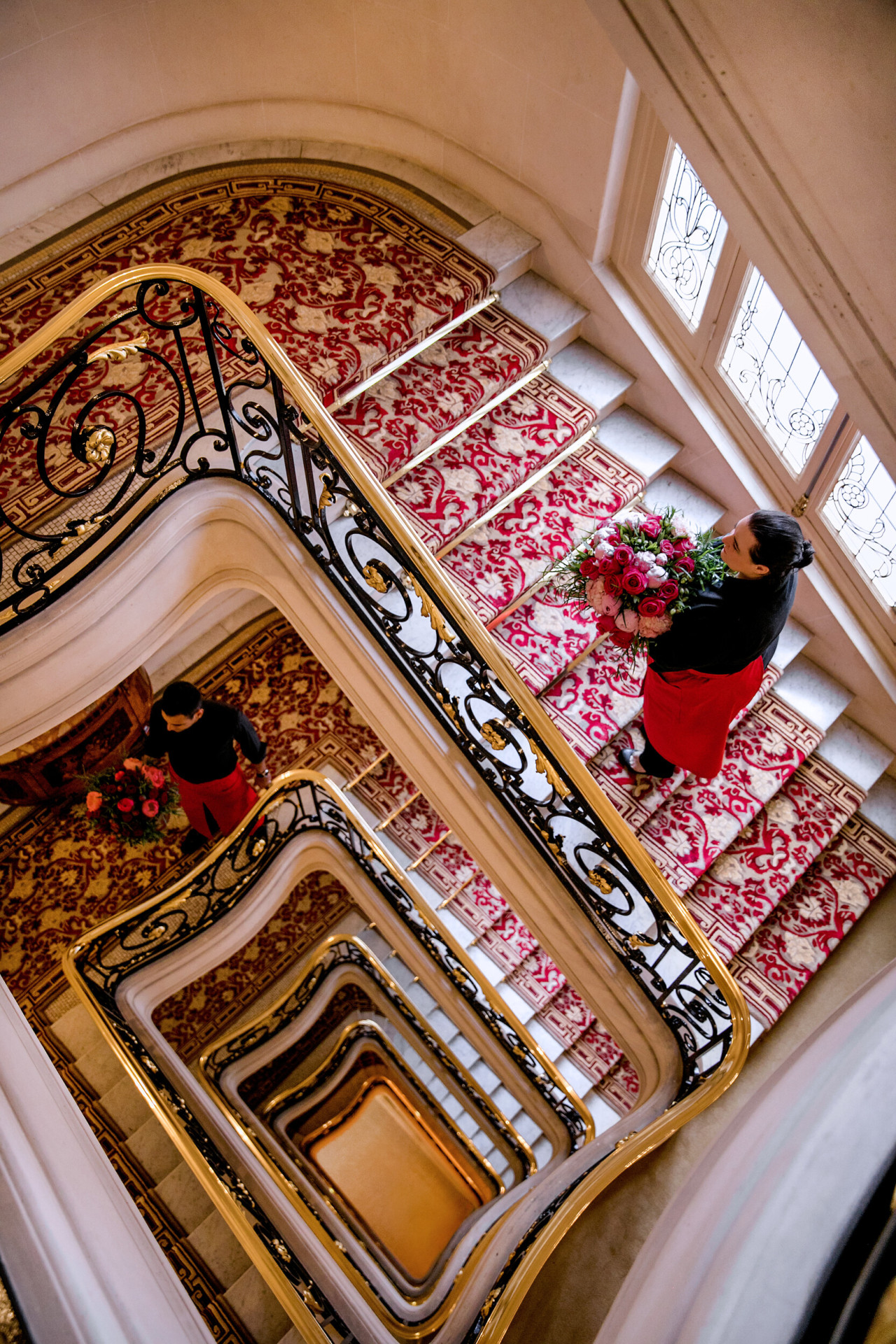 Hôtel Plaza Athénée, Paris, legendary red staircase with gold banister, and two florists holding red and pink bouquets.