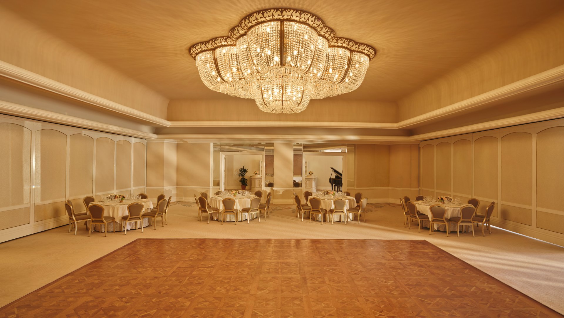 Elegant banquet hall with round tables, chairs, and a grand chandelier ceiling light.