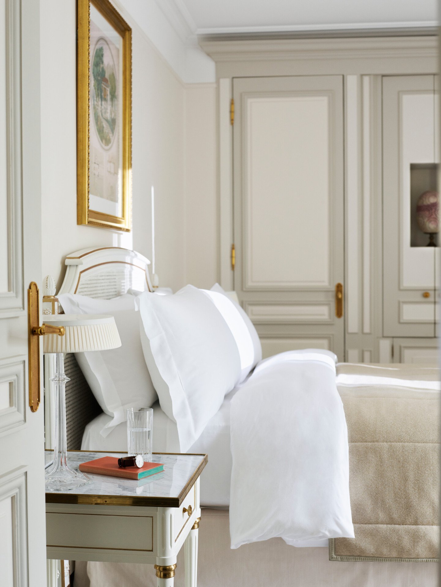Quarto em tons de bege e branco com armário de madeira ao fundo e cama queen. No Le Meurice, Paris.