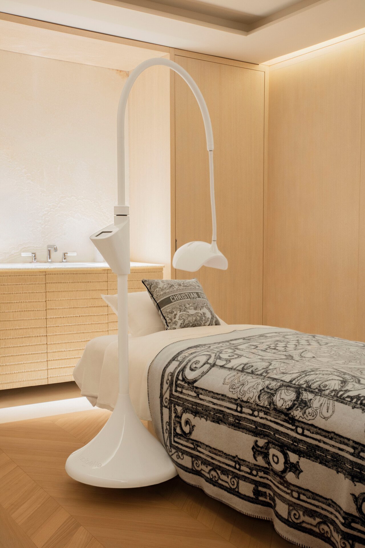 Chambre minimaliste décorée dans des tons bois clair. Elle comprend un lit avec un oreiller griffé et un couvre-lit raffiné, des suspensions élégantes au plafond et un lavabo moderne en bois.
