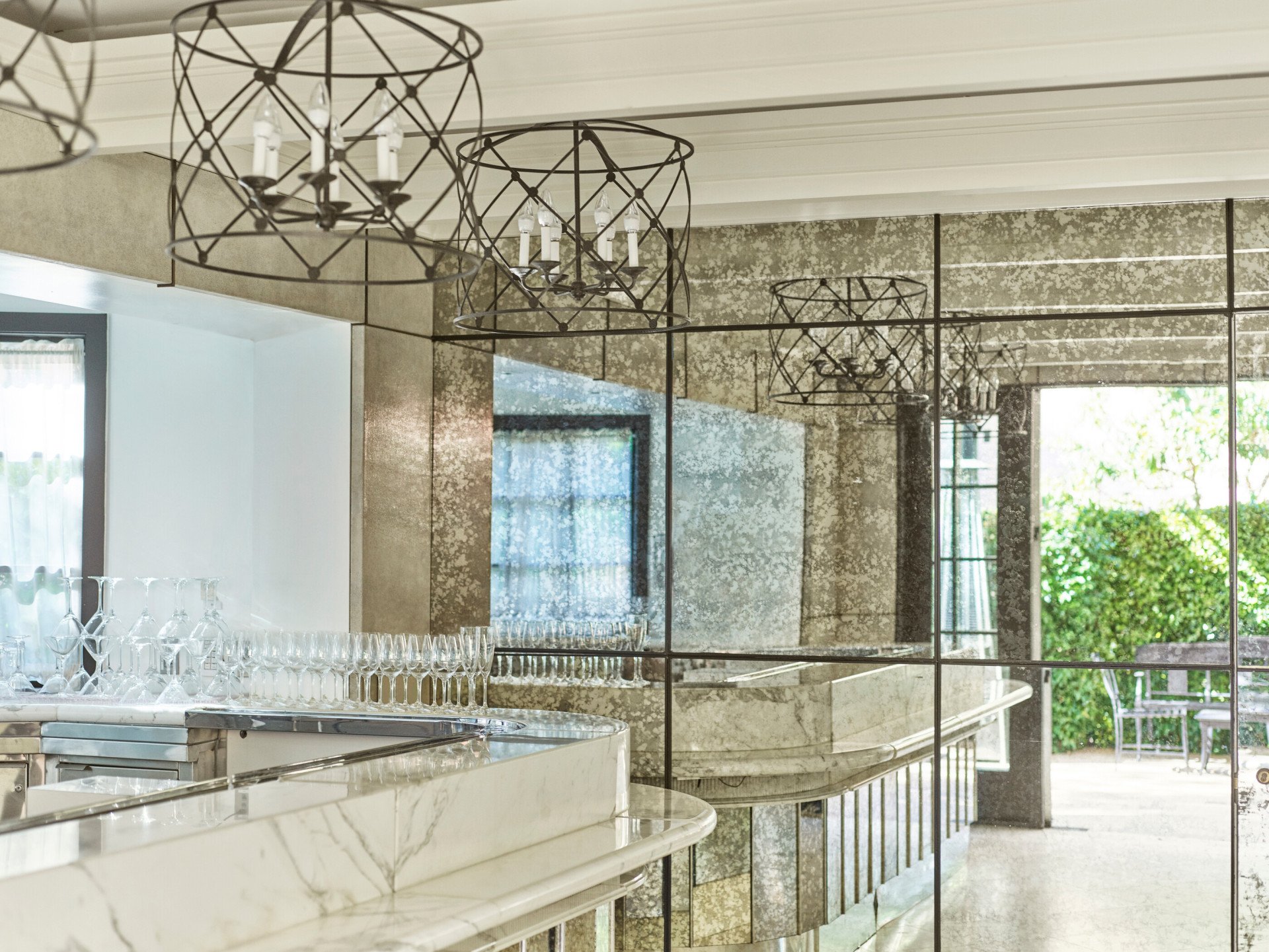 Garden foyer marble bar set up with different types of glasses, being reflected in a vintage mirrored wall at Hotel Bel-Air