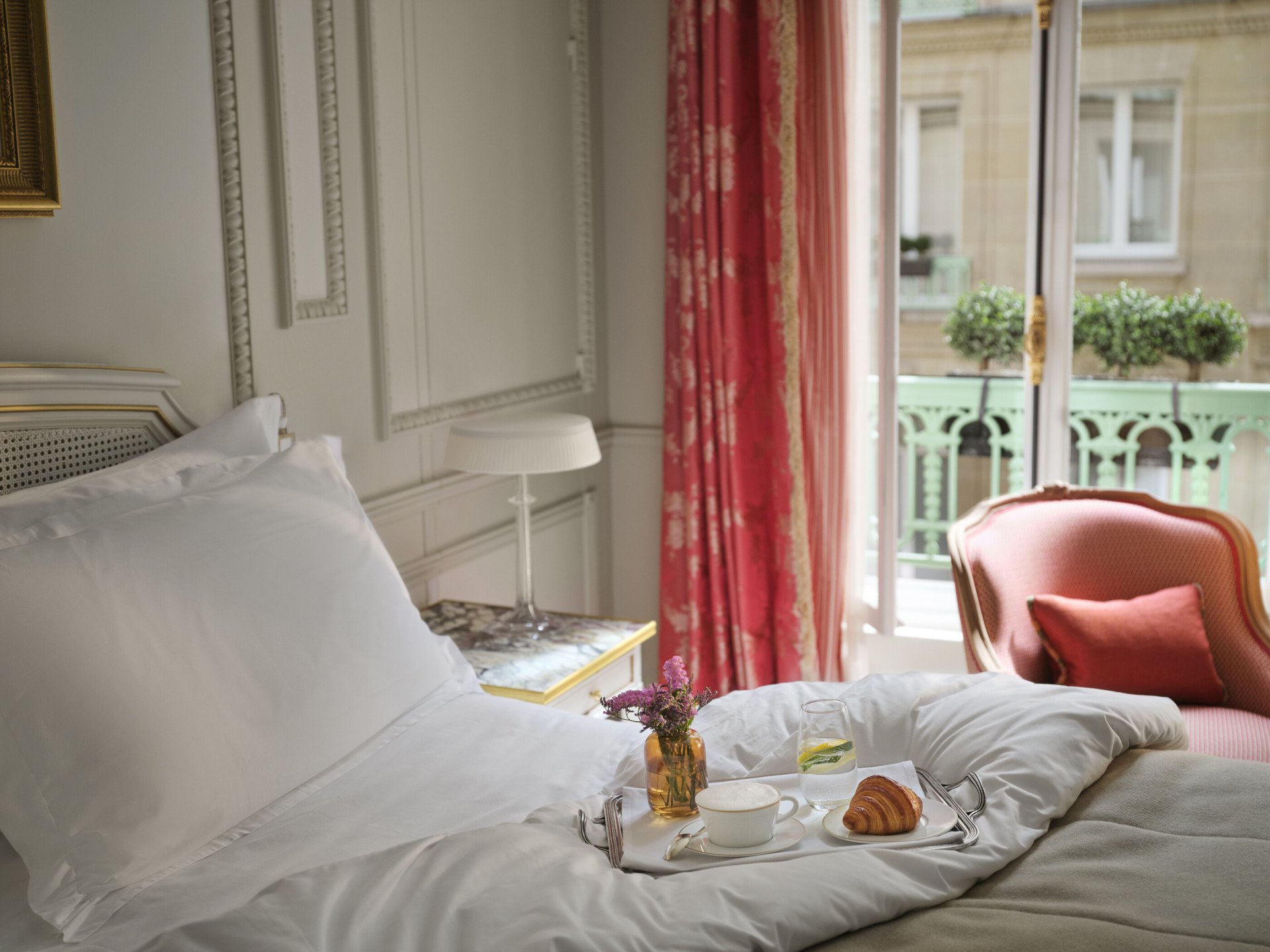 Fotografia da parte superior da cama com um tabuleiro de pequeno-almoço em cima, com uma chávena de café, um croissant e um arranjo de flores, no Le Meurice, Paris