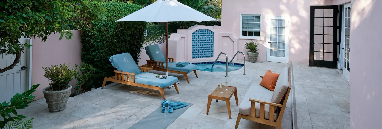 Full view of the patio in the legendary Chalon Suite with outdoor jacuzzi, two lounge chairs with an umbrella covering them, and a small side table with two glasses of champagne on top.
