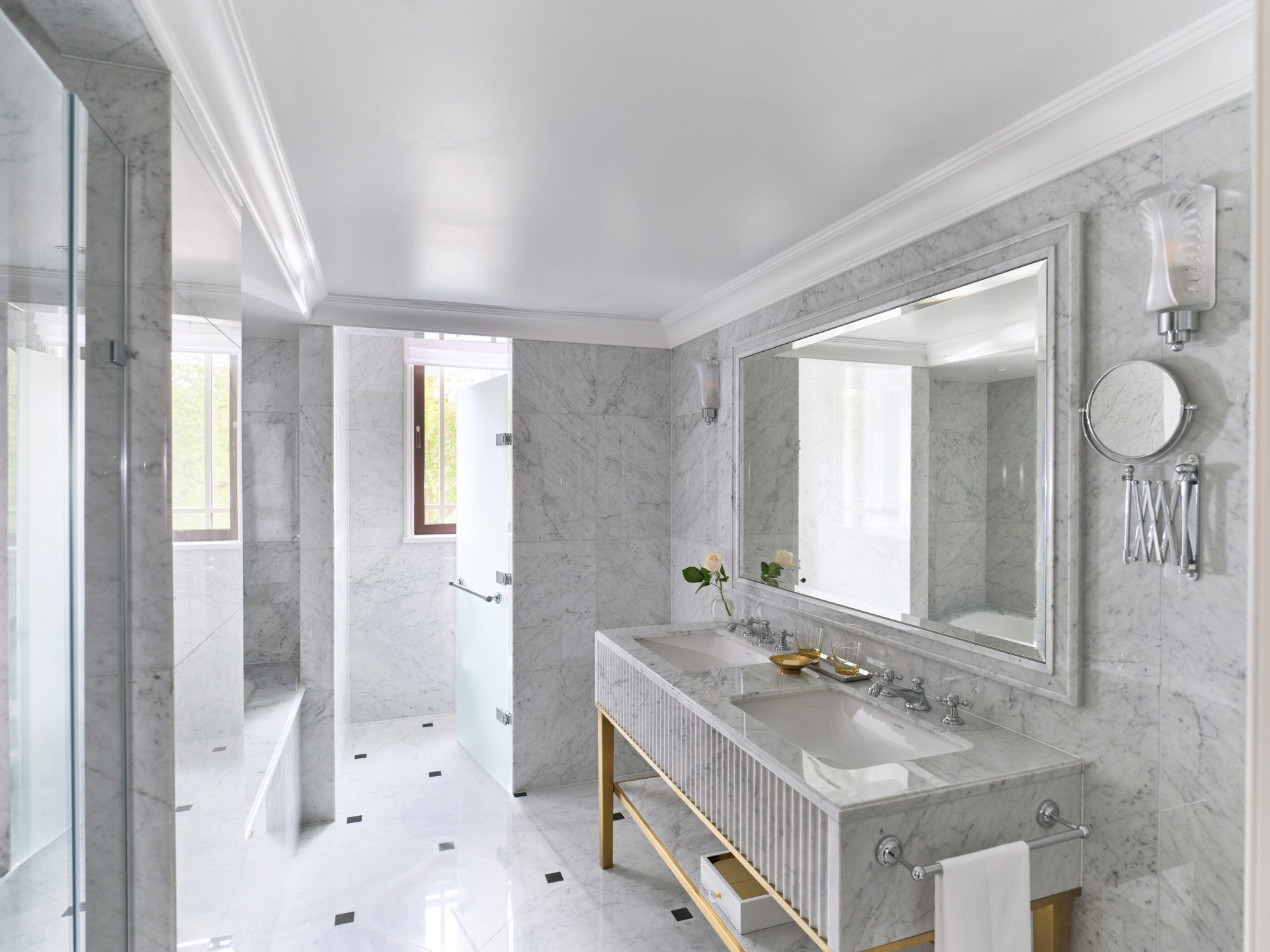 The Deluxe Park View Room bathroom at The Dorchester, showcasing floor-to-ceiling marble, a double vanity with gold detailing, a large mirror and a walk-in shower.