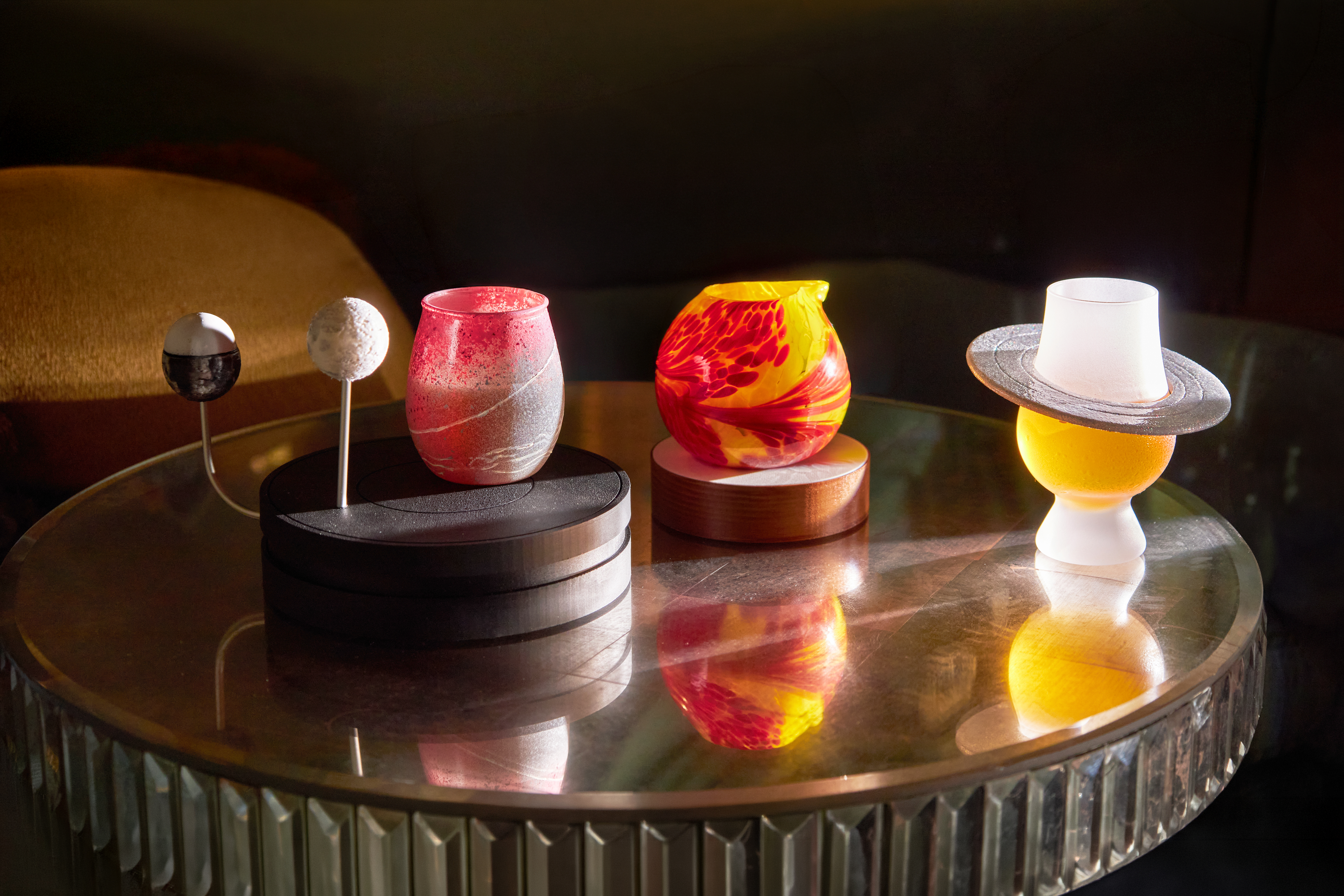 A selection of cocktails and presentation elements from The Vesper Bar’s Planetarium menu, displayed on a reflective table with sculptural glass vessels and celestial-inspired details.