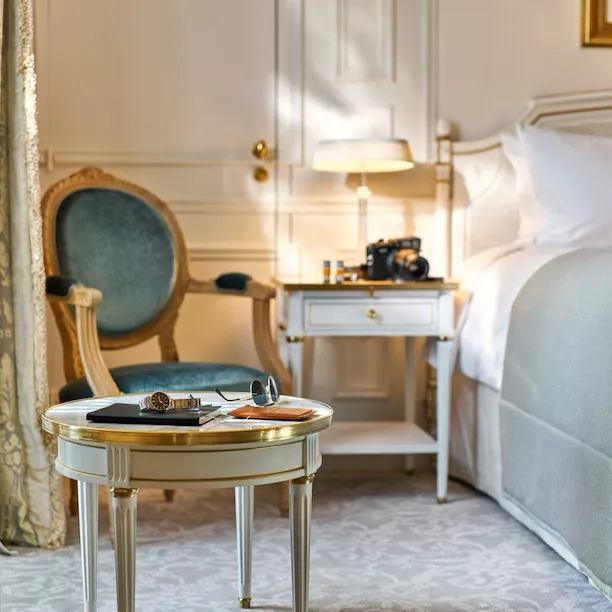 Óculos de sol, um relógio e um bloco de notas colocados numa mesa junto à cama num quarto executivo. No Le Meurice, Paris.