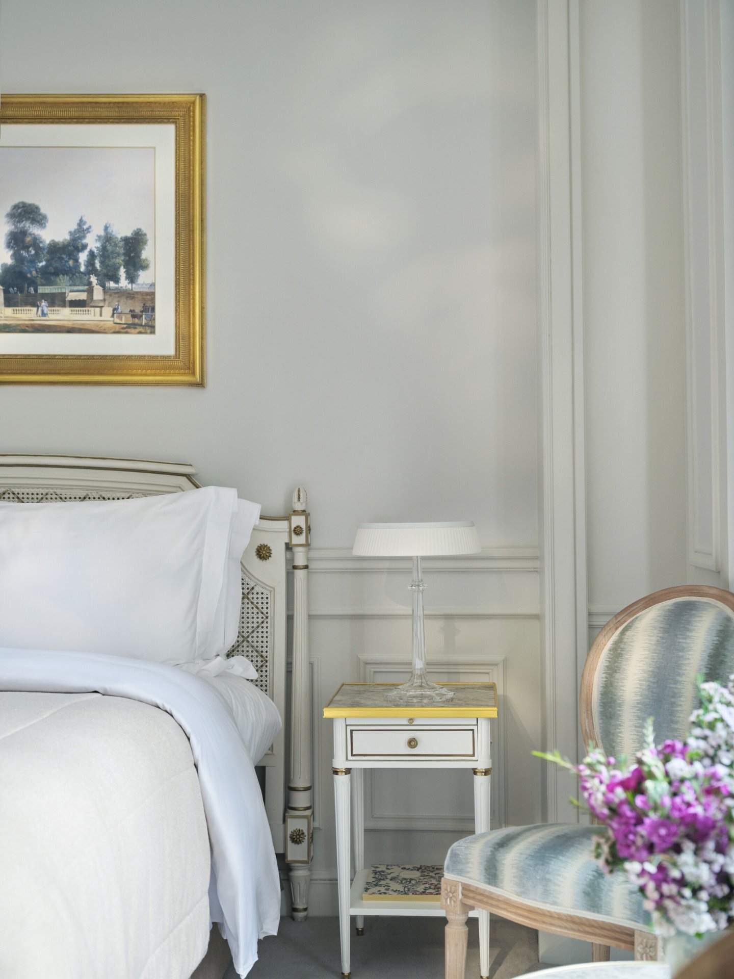 imagem centrada no lado esquerdo da cama com os pormenores das flores e uma cadeira, em Le Meurice, Paris