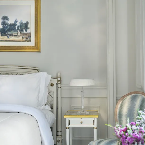 imagem centrada no lado esquerdo da cama com os pormenores das flores e uma cadeira, em Le Meurice, Paris