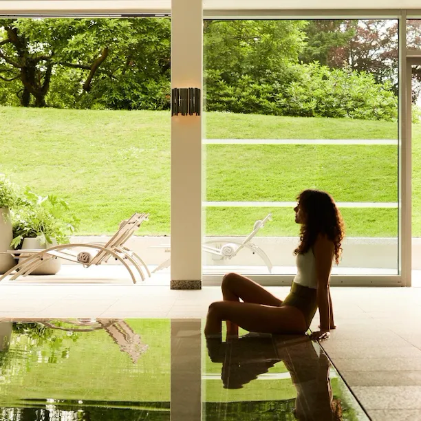 Guests enjoying the pool at Coworth Park with beautfiul light flooding through the open doors to the lush green forest and hills
