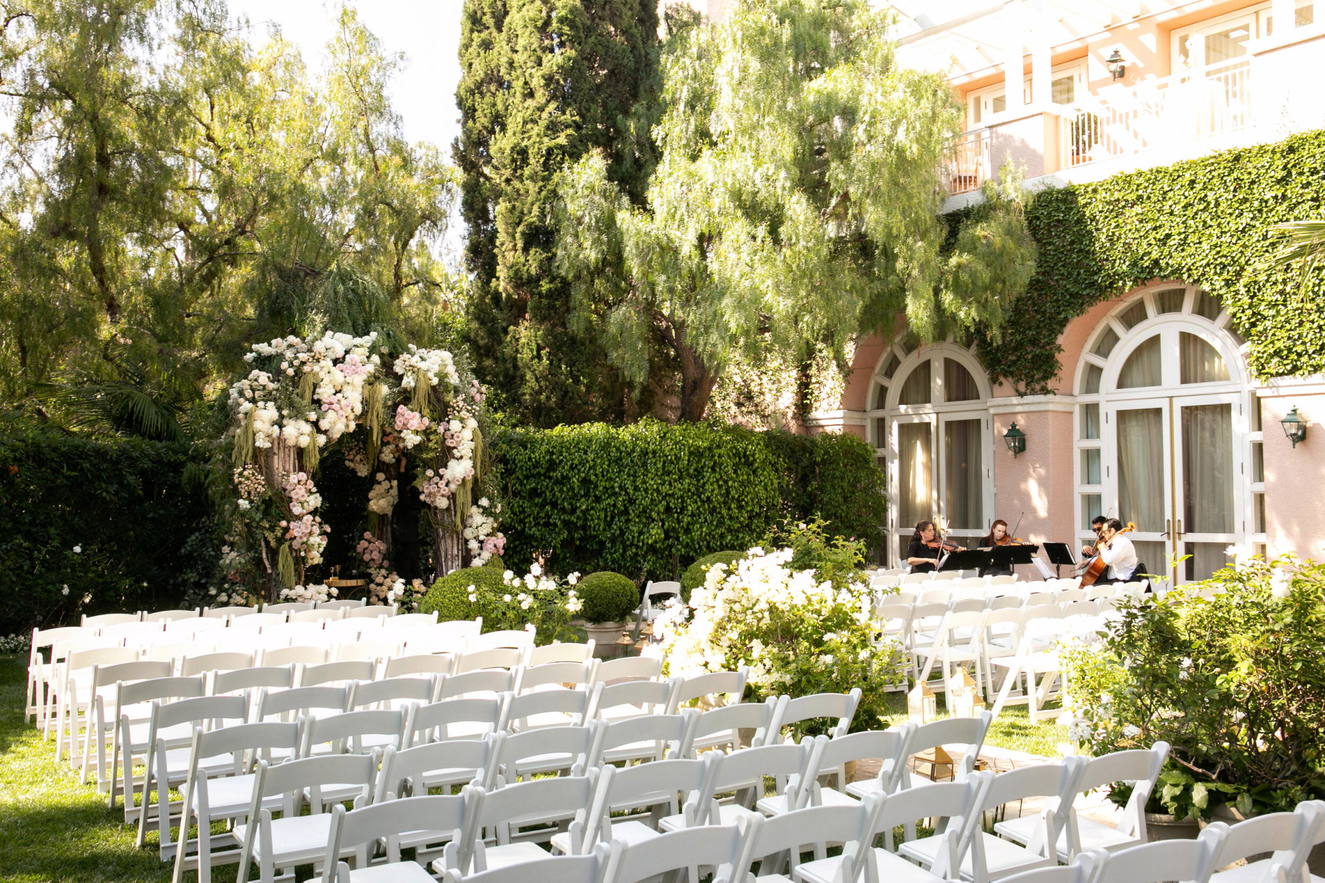 White chairs set for a afternoon wedding ceremony outdoors in the crystal garden while musicians warm up