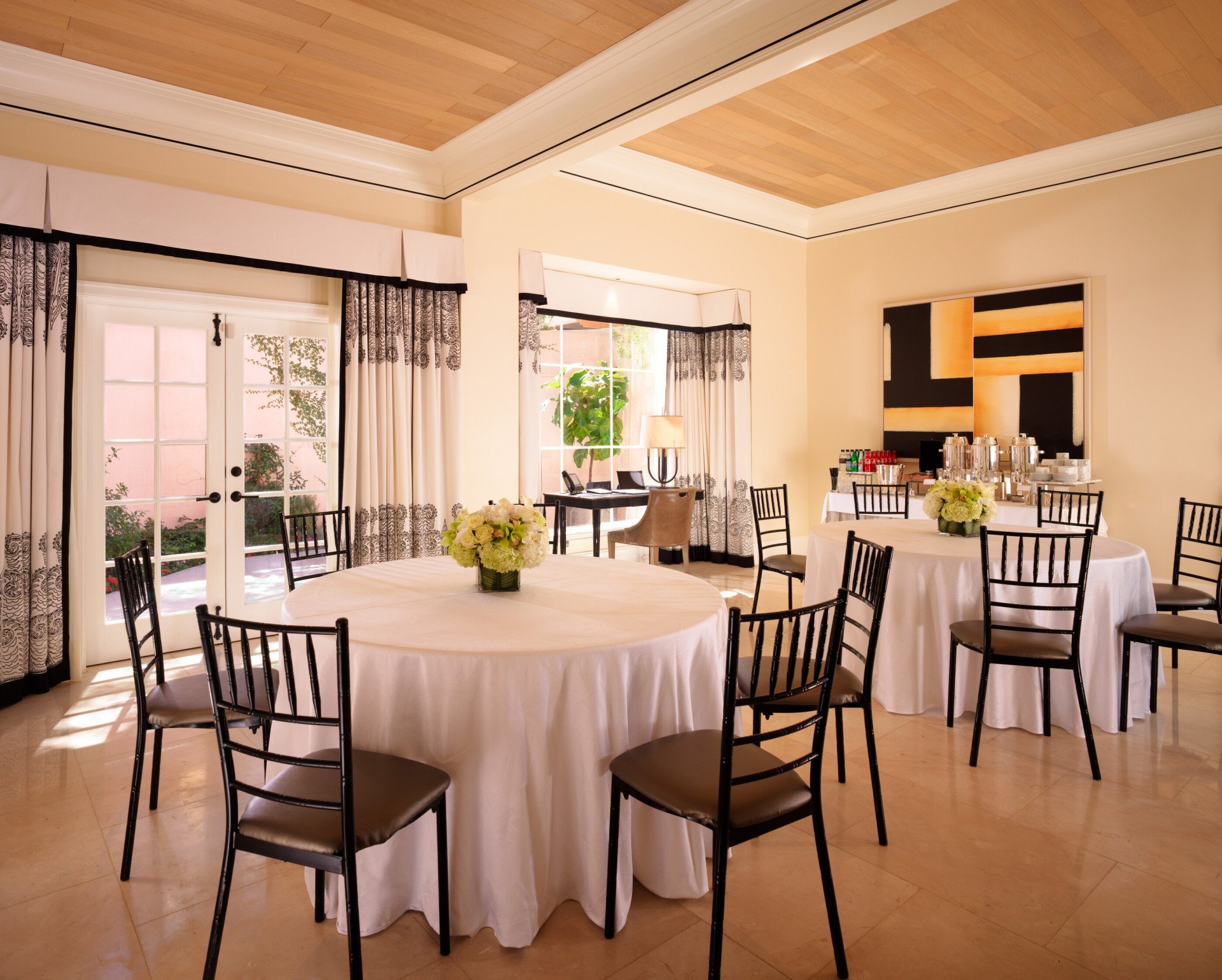 Three round tables and chairs with floral centerpieces set up inside a bright, spacious Hospitality Suite 