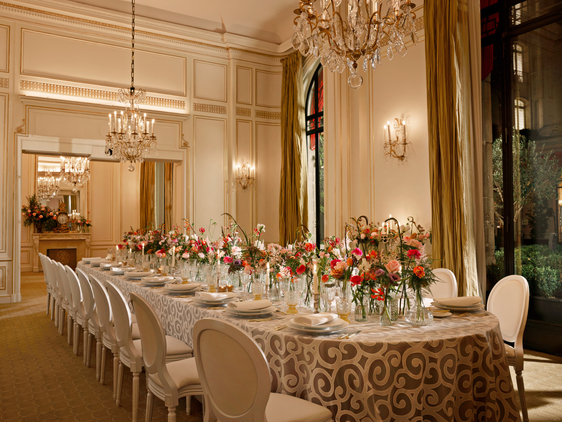 Uma longa mesa posta com uma toalha de mesa cinzenta e flores multicoloridas no Salon Organza no Hôtel Plaza Athénée, Paris - Dorchester Collection.