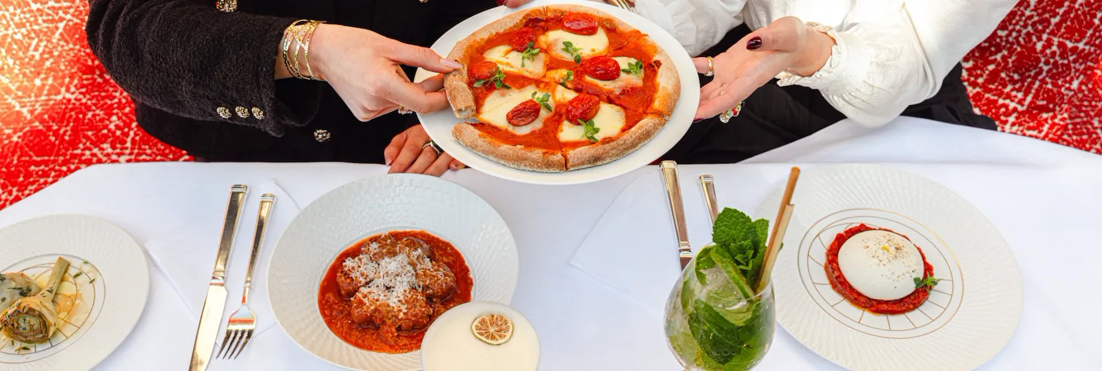 Two people share a pizza at a festive table with drinks and desserts.