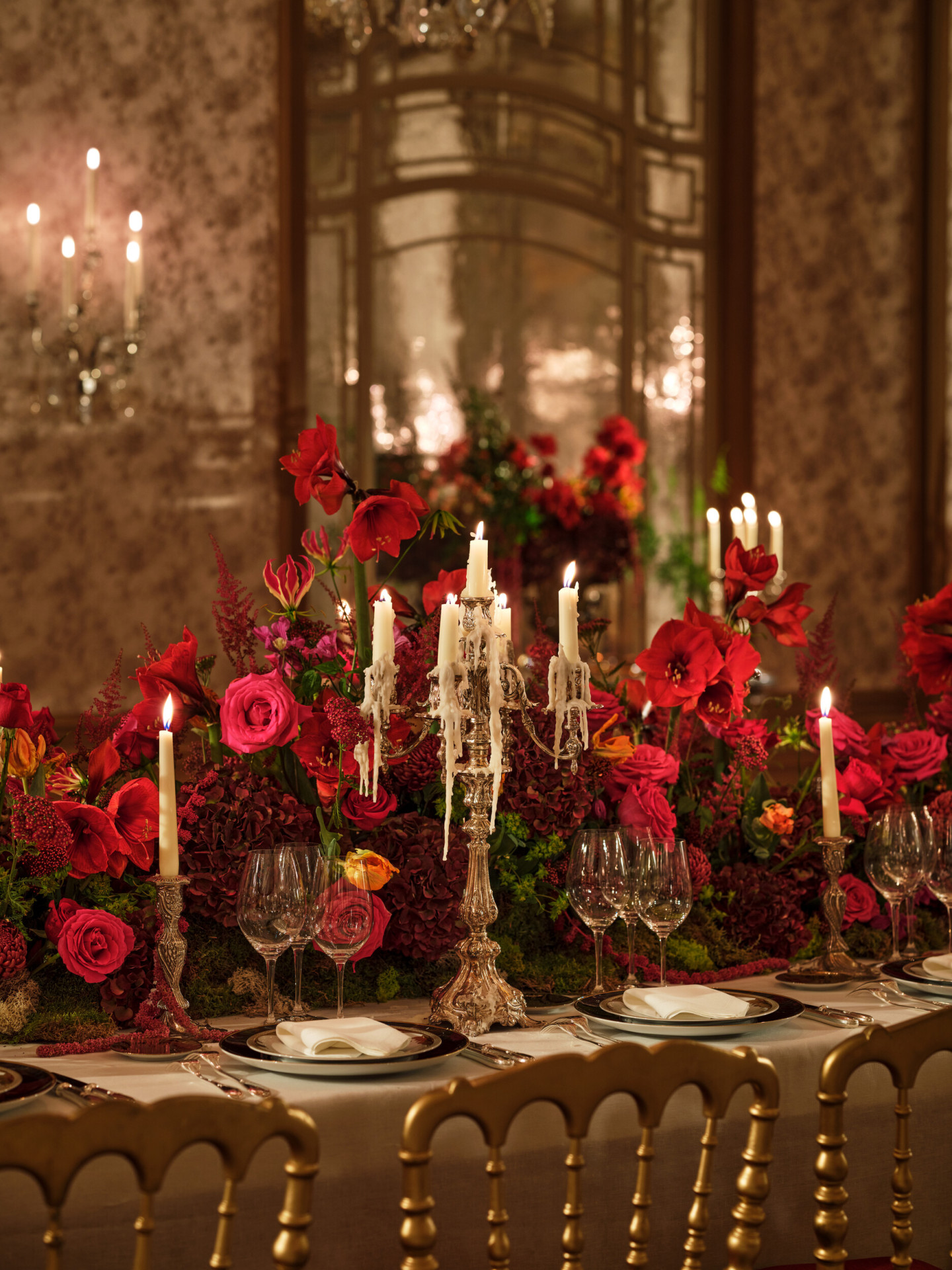 Une élégante table à manger ornée de fleurs rouges éclatantes et de candélabres décorés de cire coulante. Des verres et des assiettes en cristal ajoutent une touche de luxe à la scène.