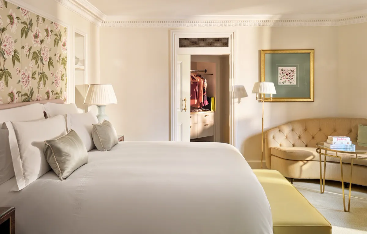 Interior of The Dorchester Studio with a king-sized bed, floral wall panel, upholstered sofa, side table and an adjoining dressing area visible through an open doorway.