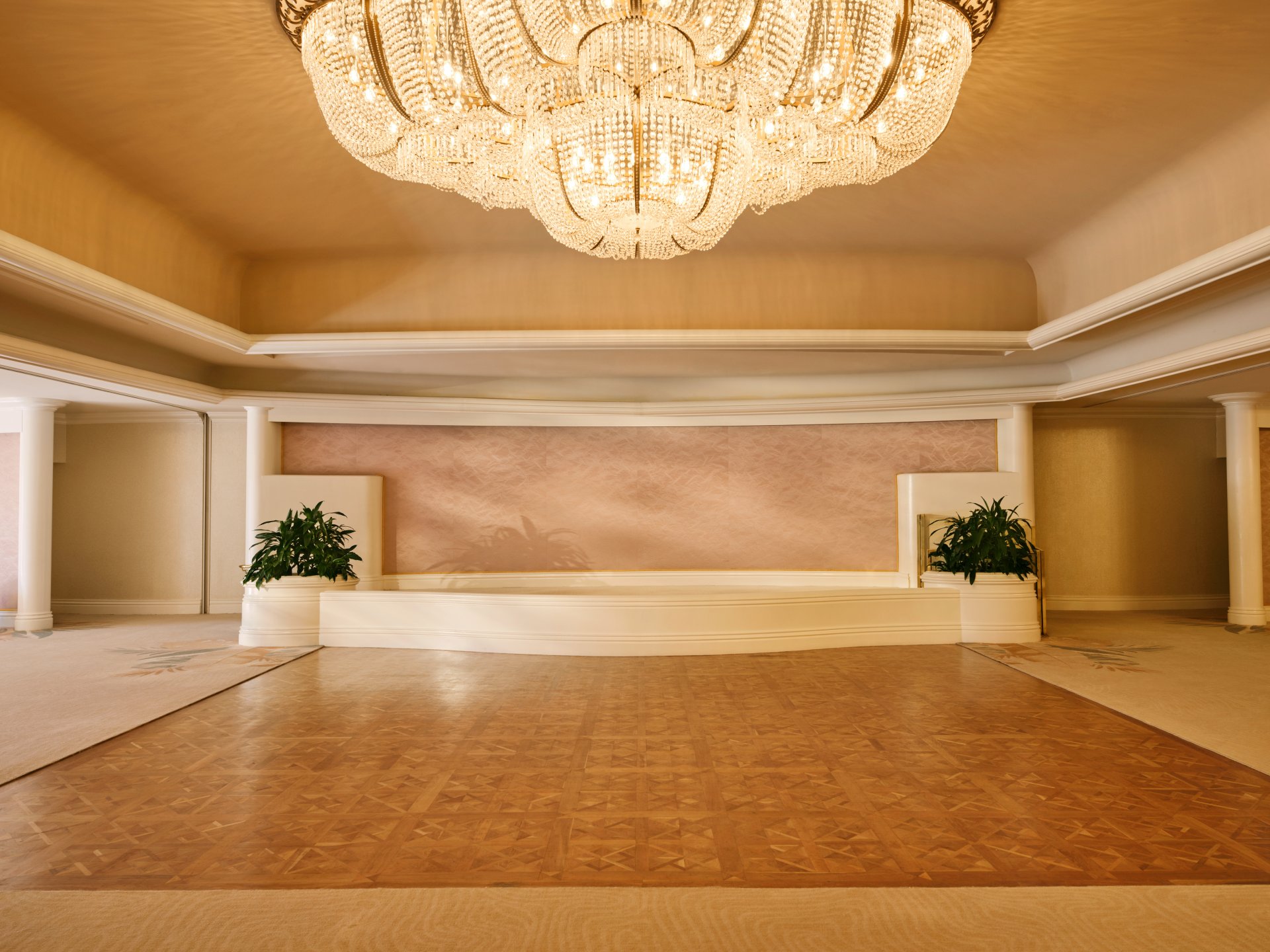 Empty elegant banquet hall with chandelier and plants, ready for an event or gathering.