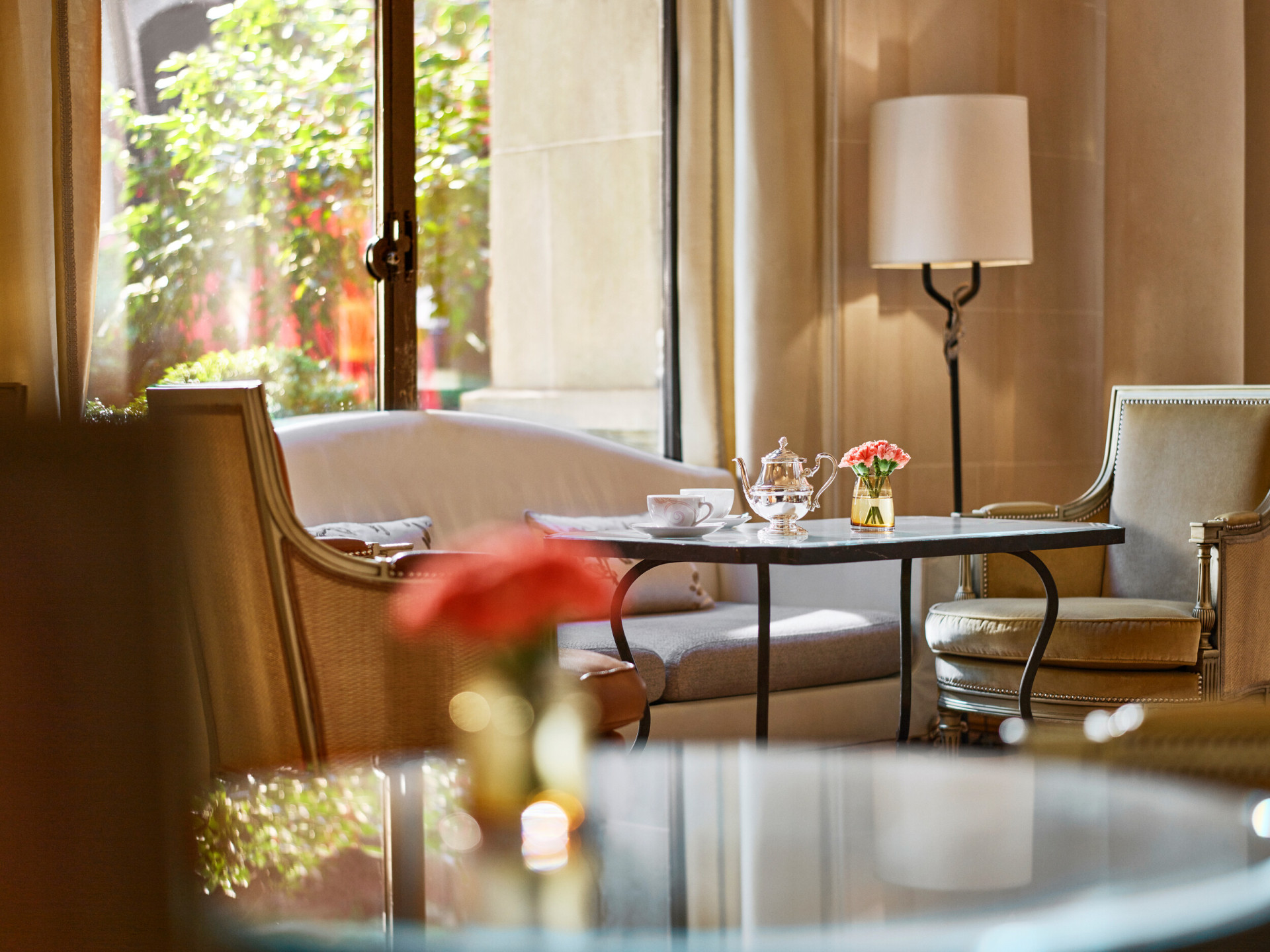 Grande plano de uma mesa de jantar na galeria, mesa com chávenas de chá, dois cadeirões e um sofá junto a uma janela solarenga, no hotel Plaza Athénée, Paris