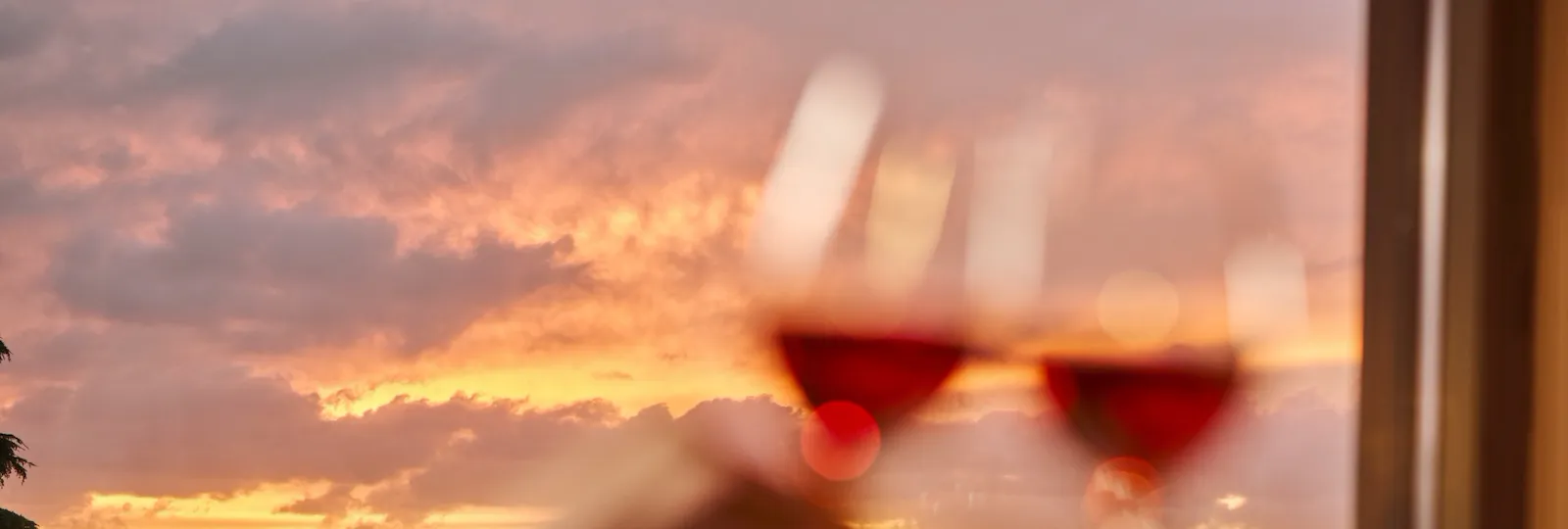 Two glasses of wine clink with a sunset view over a city skyline, creating a romantic mood.