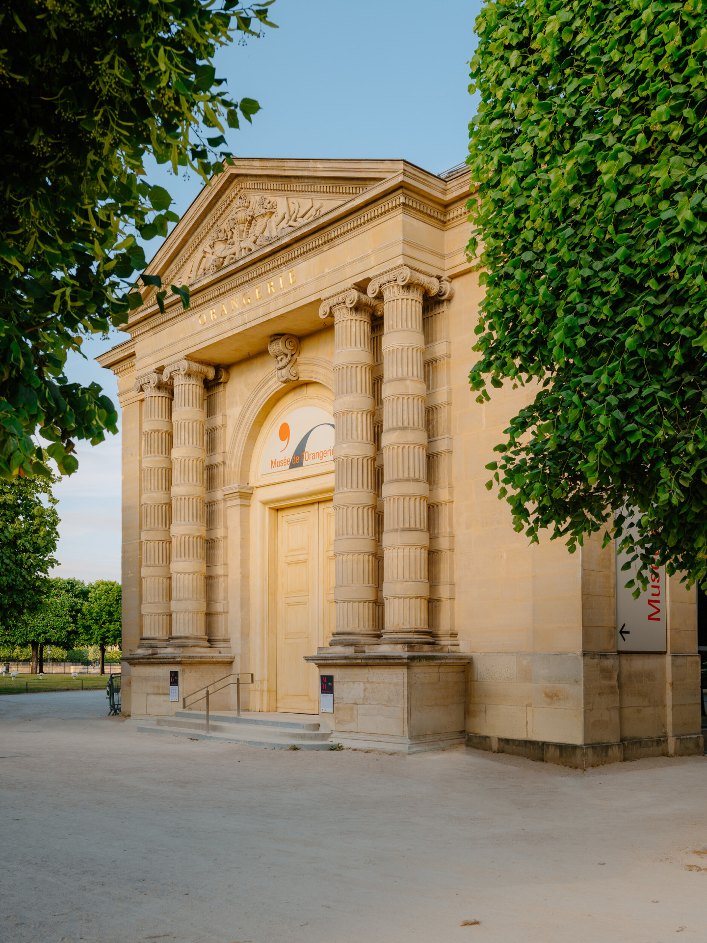 Photo de l’entrée du musée de l’Orangerie avec des arbres autour et un ciel bleu ensoleillé, au musée de l’Orangerie, Paris. 