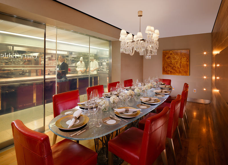 Chef's Table private dining area with view into the kitchen. Table set for 10 peope with gold and white table settings and floral arrangements. 