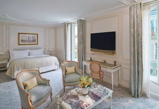 Large view of a Deluxe Junior Suite with the stone marquetry on the table and the TV and the Bed on the background, at Le Meurice, Paris