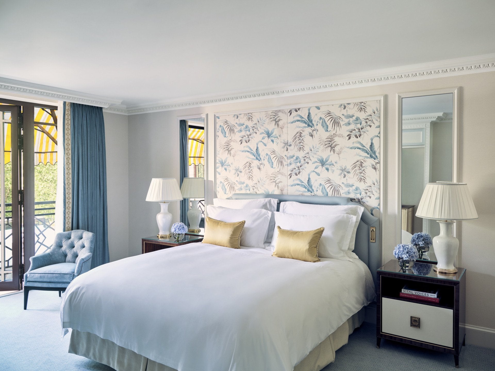 The Executive Park View Room at The Dorchester, showcasing a king-sized bed framed by blue botanical wall panels, classic bedside tables, soft blue accents and French doors opening towards Hyde Park views.