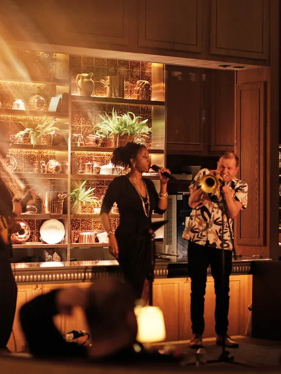 Live music at Ronnie Scott’s at The Dorchester, showcasing musicians performing on stage in front of a mirrored back bar, with warm lighting and guests seated throughout the intimate venue.
