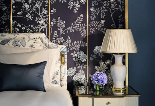 Bedroom detail in The Regal Suite with a floral decorative wall panel, blue walls, a bedside lamp, fresh hydrangeas and an upholstered headboard.