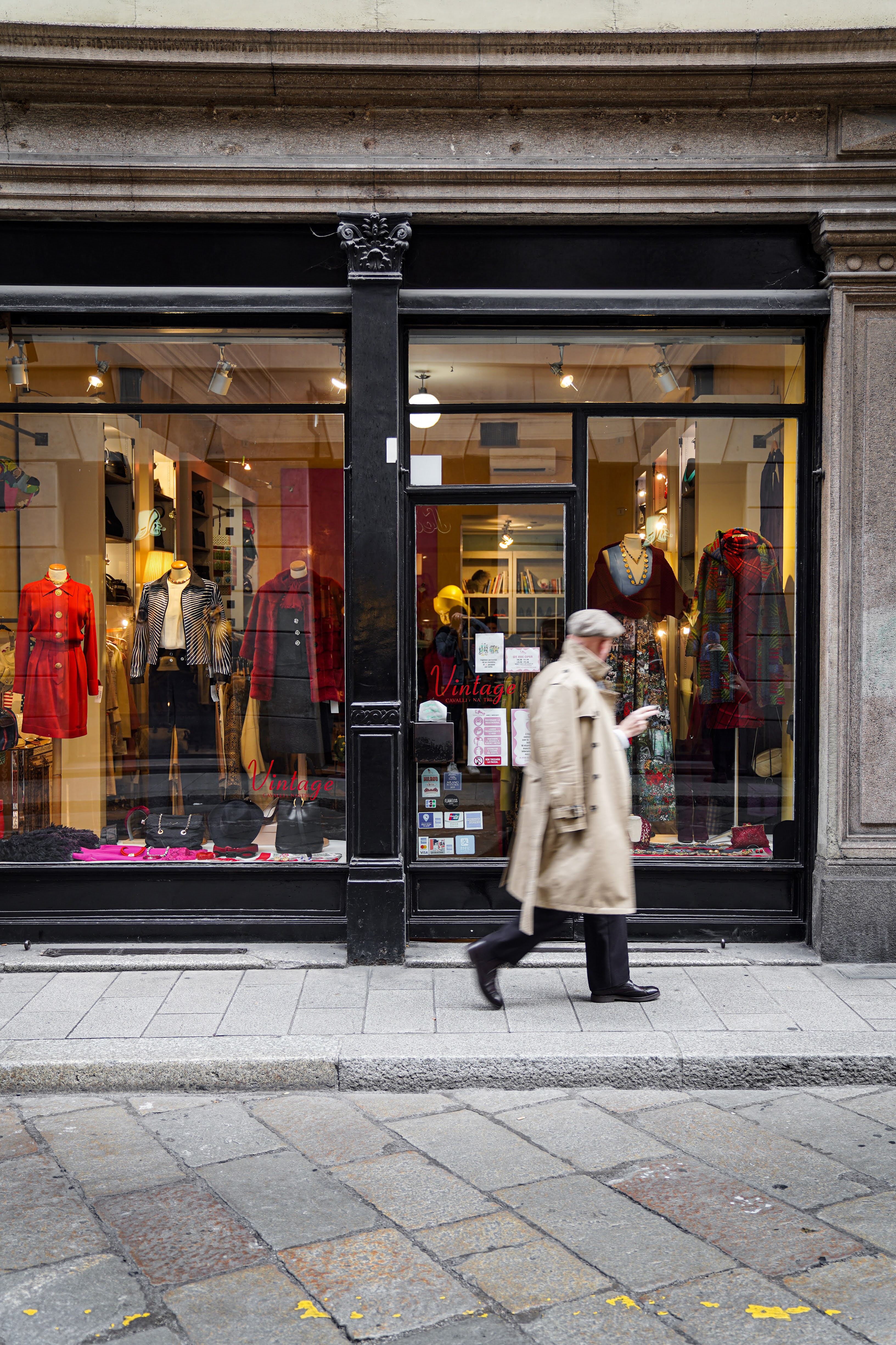 window of "Cavalli e Nastri", one of Milan’s most celebrated vintage stores, with a man walking in front wearing a beige raincoat