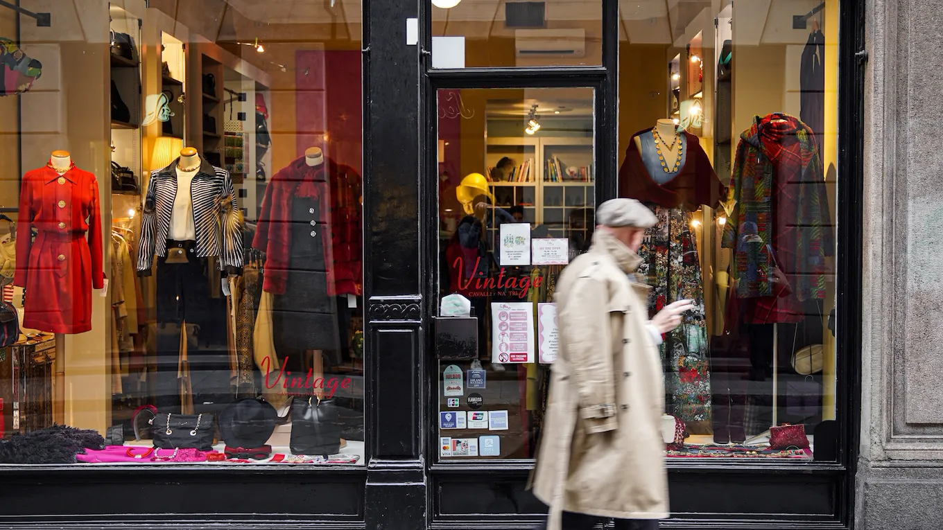 window of "Cavalli e Nastri", one of Milan’s most celebrated vintage stores, with a man walking in front wearing a beige raincoat