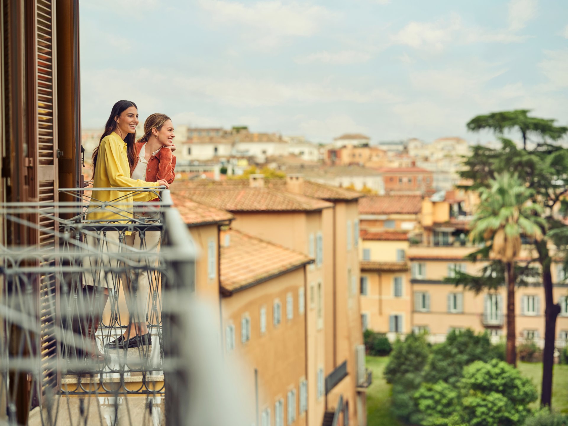 Due giovani donne sorridenti che ammirano la vista su Roma da un balcone di Hotel Eden