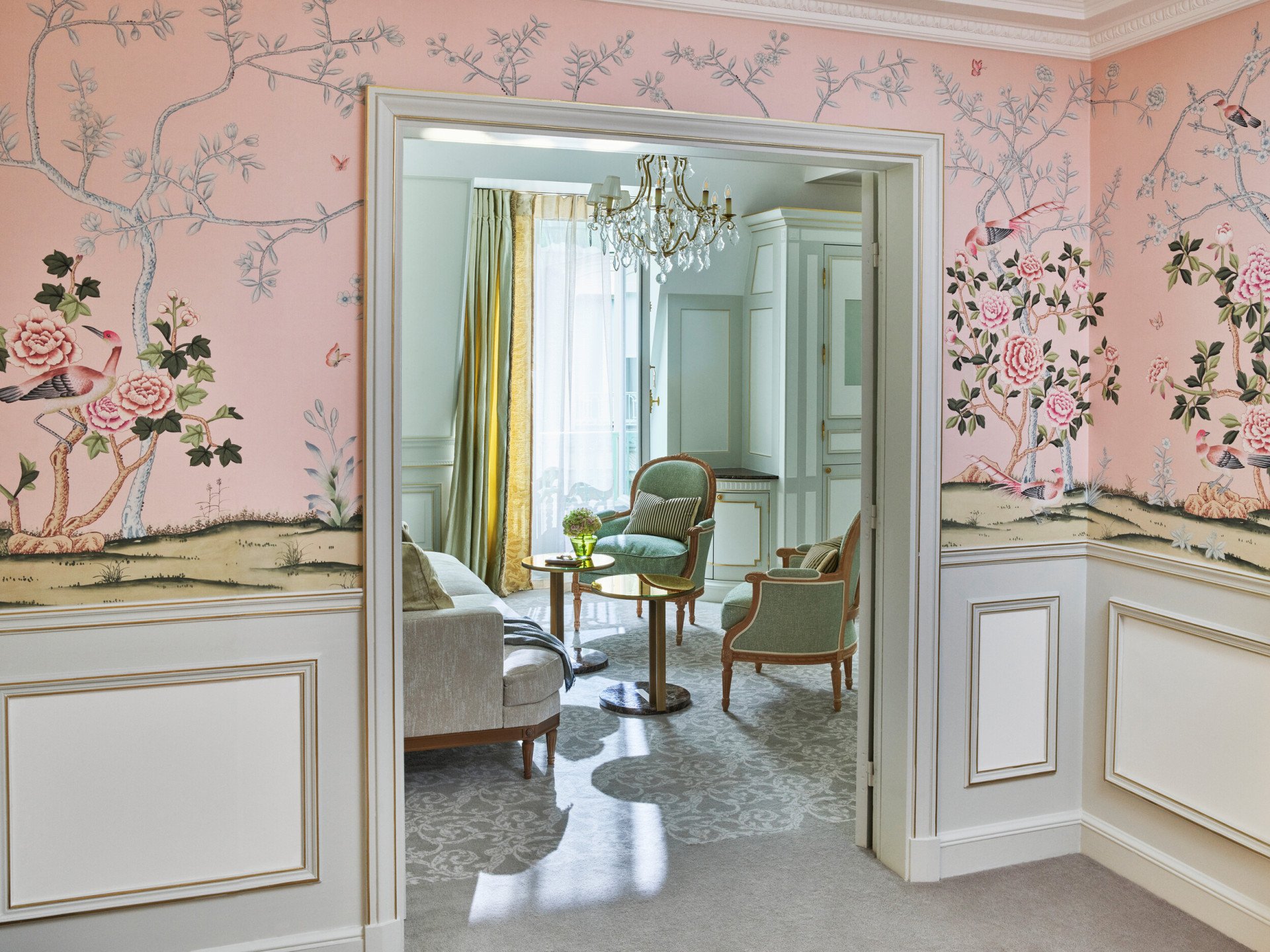 Vue lointaine du salon, mettant en valeur le papier peint rose de la chambre, au Meurice, Paris.