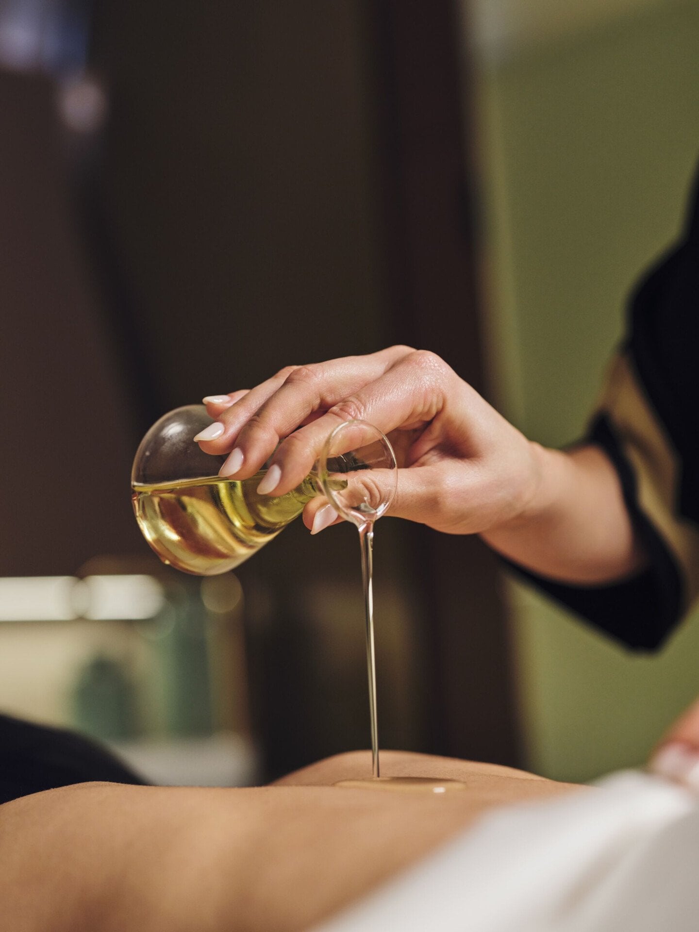 Spa therapist pouring massage oil on the back of a lying woman