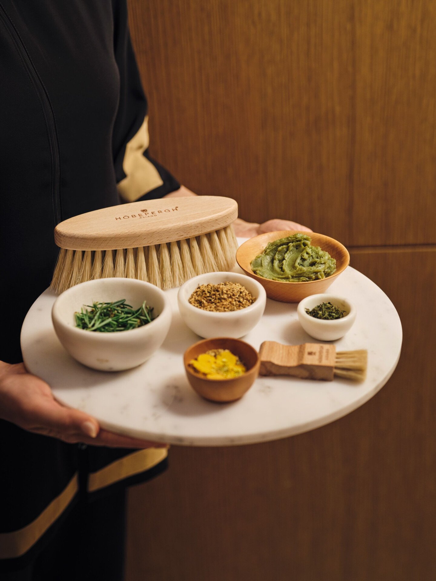 Spa therapist holding tray with brushes, small bowls with alpine herbs