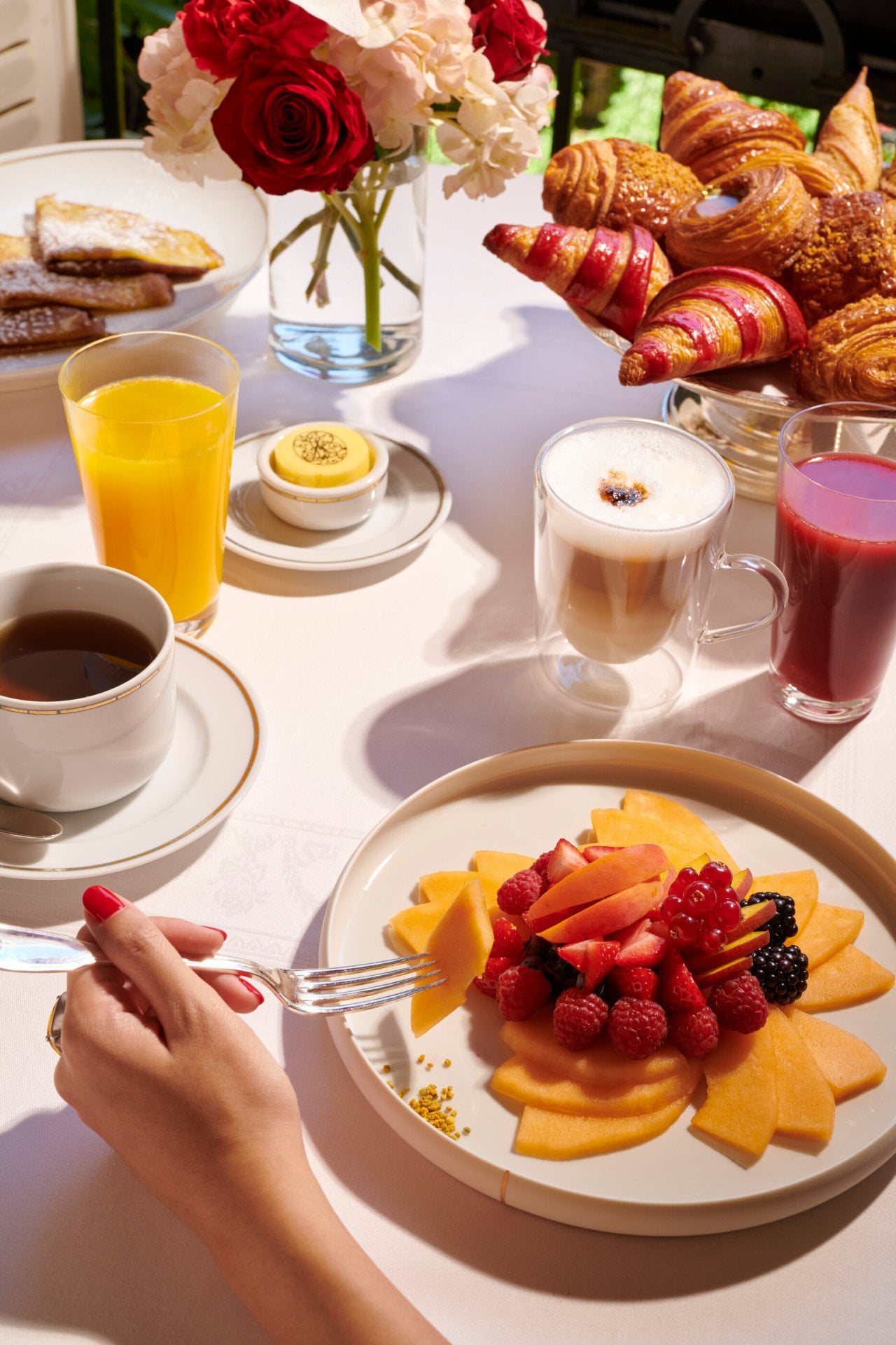 Images du brunch au Jean Imbert au Plaza Athénée. On peut voir une main qui cueille des fruits dans une assiette de salade de fruits.
