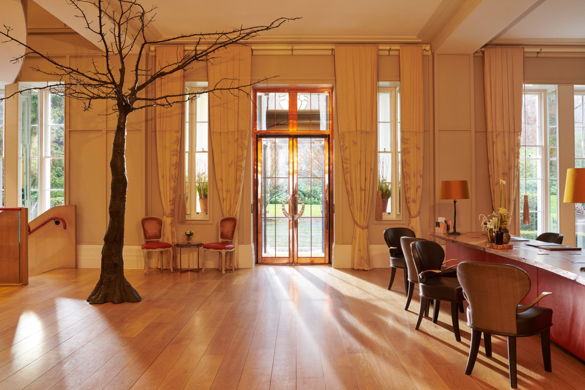 Entrance lobby doors and reception desk with sun streaming in at Coworth Park, Ascot