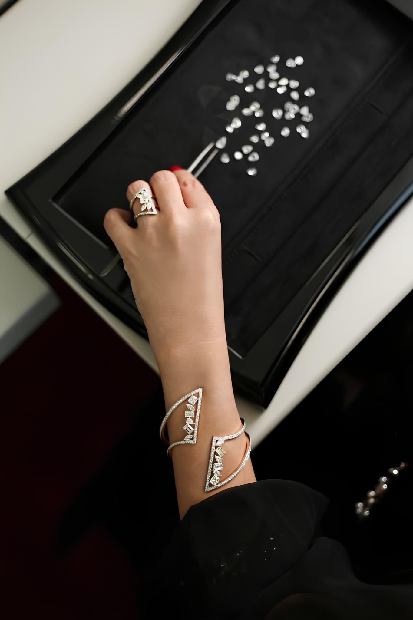 A close-up of a woman's left hand selecting a diamond from a jewelry tray