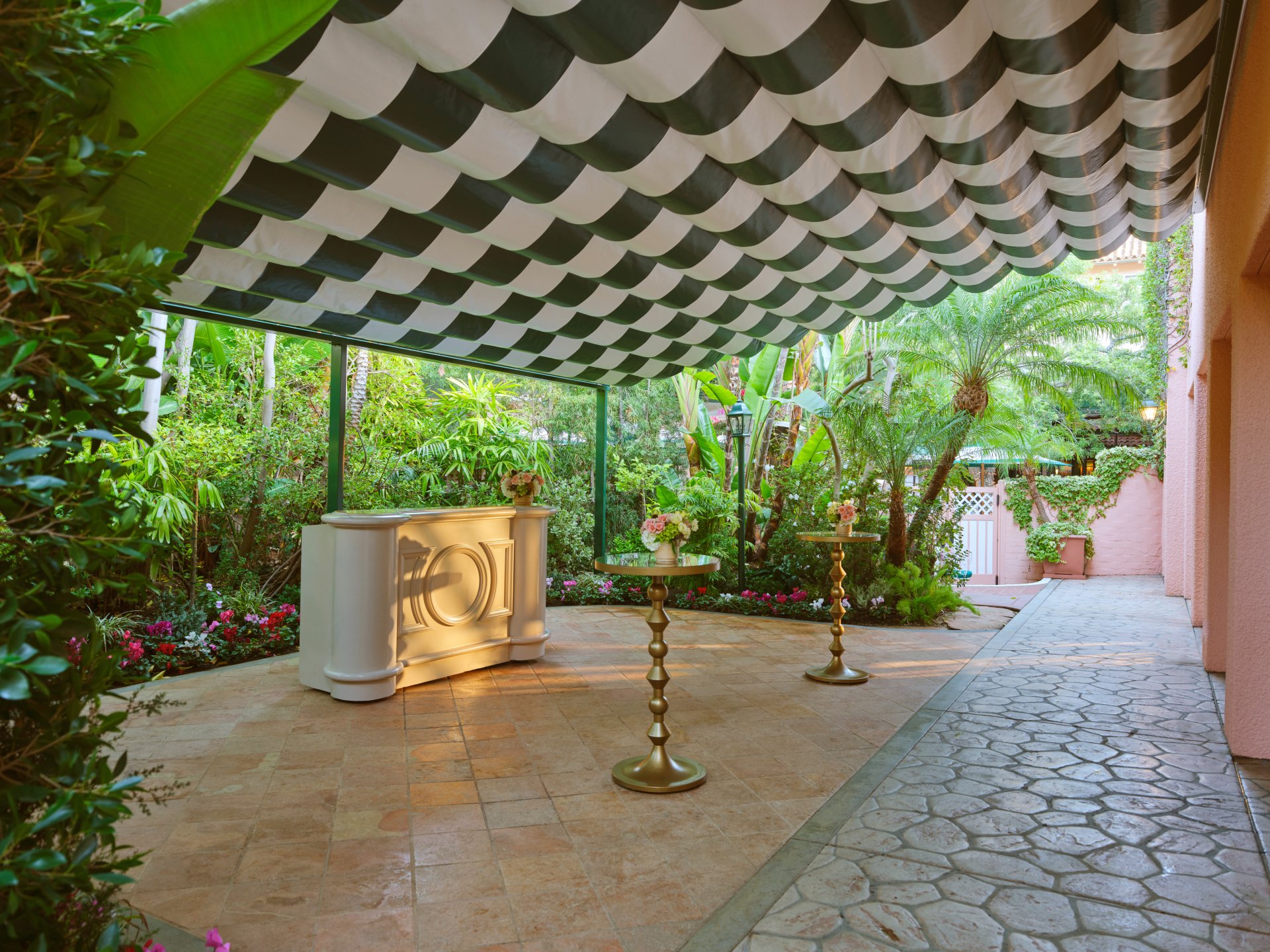 Outdoor garden with columns, plants, and a shaded seating area under a striped awning