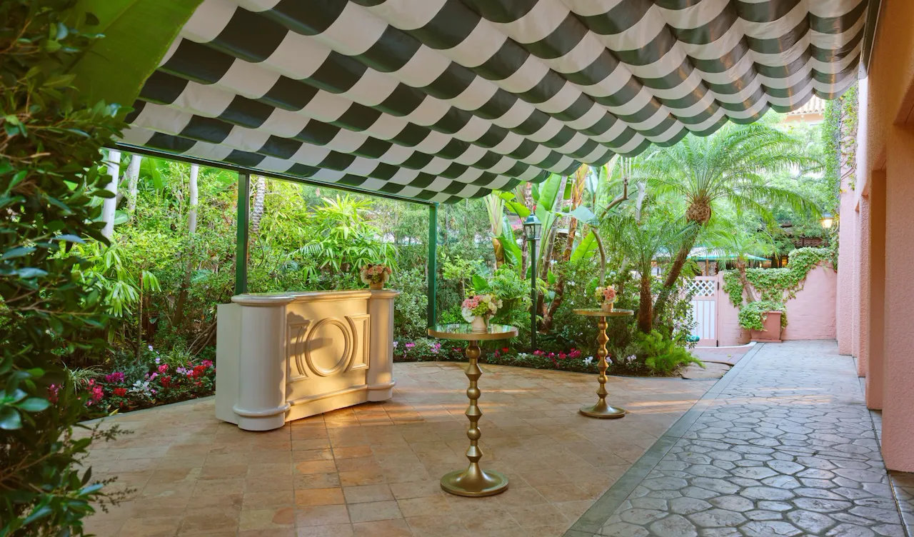 Outdoor garden with columns, plants, and a shaded seating area under a striped awning