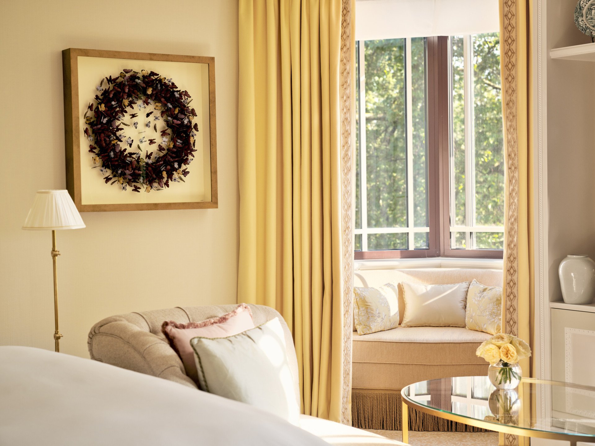 The Dorchester Suite at The Dorchester, featuring warm yellow interiors, elegant seating and a large bay window with a built-in window seat overlooking Hyde Park.