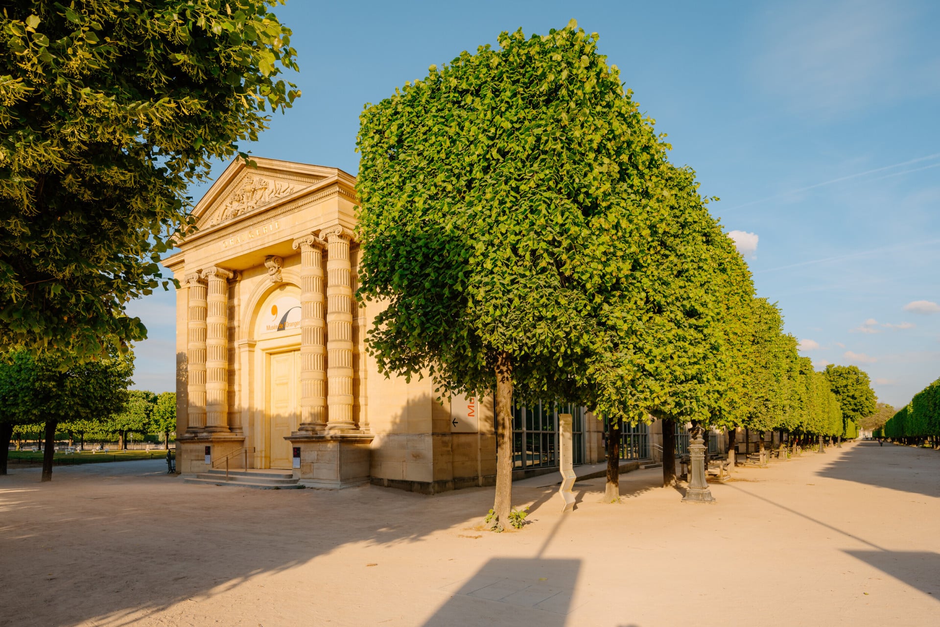 Entrance of the Musée de l'Orangerie with an alley of trees and a sunny blue sky, at Musée de l'Orangerie, Paris. 