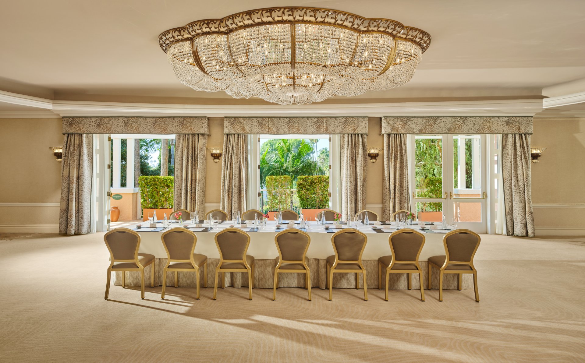 Elegant empty banquet room with large windows and a long table under a grand chandelier