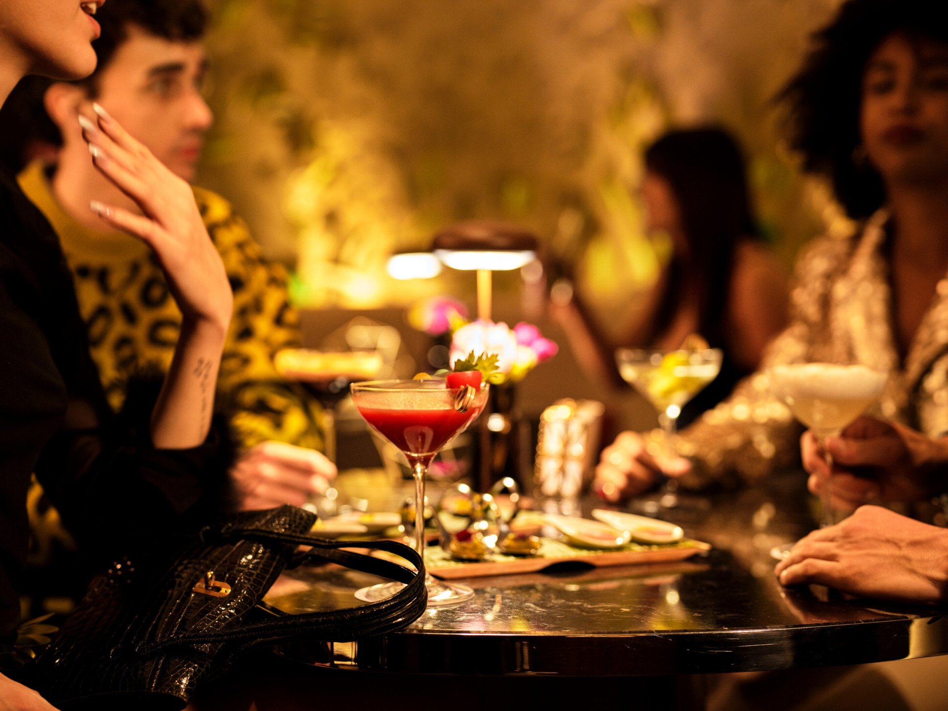 Un gruppo di giovani donne e uomini con cocktail e cicchetti seduti ad un tavolo de Il Giardino bar, a Hotel Eden